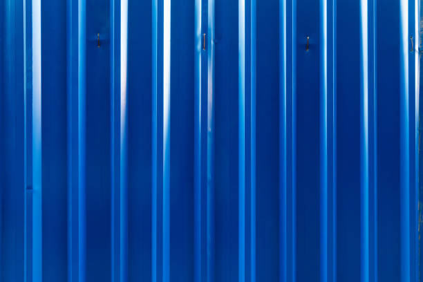 A close-up view of a corrugated metal wall painted in a vibrant blue color. The surface features vertical ridges and subtle reflections of light, creating a dynamic and modern texture. Ideal for use as a background or industrial-themed design element.