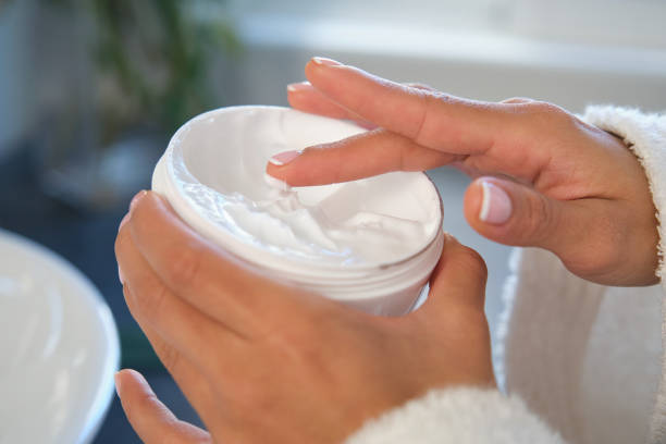 Woman dipping finger into jar of moisturizing cream for her face, body care and wellness
