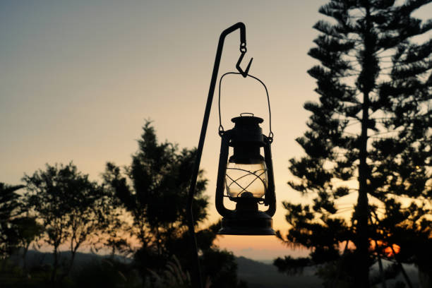 A lantern is lit up in the dark. The lantern is on a tripod. The tripod is on the ground. camping outdoor lifestyle concept.