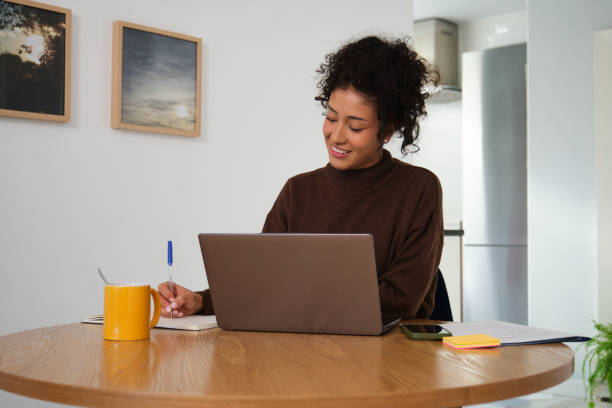 istock Young woman working from home taking notes while looking at laptop 2189419795