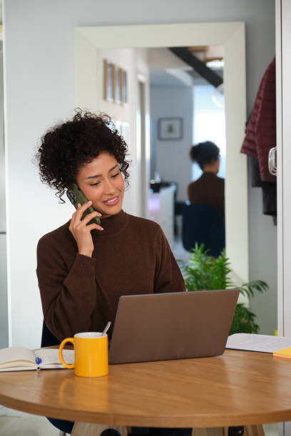 istock Young woman working from home talking on the phone and using laptop 2189419971