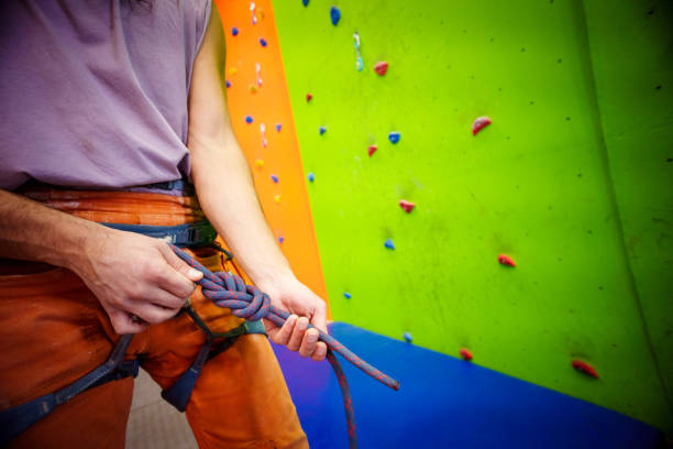 Young brunette male with long black hair works during climbing sessions on vertical walls in a sport climbing gym