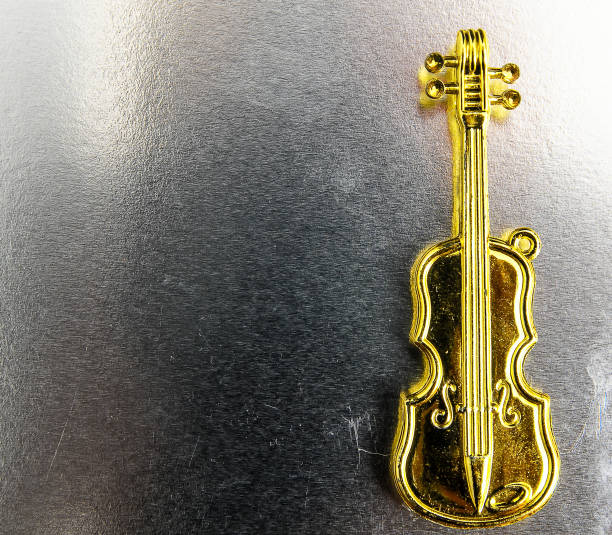 A gold violin charm is hanging from a silver surface. The shiny gold color of the violin contrasts with the silver surface, making it stand out
