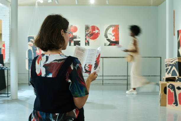 Young woman with dark straight hair looking through information about exhibition events in brochure in gallery hall