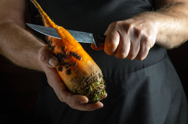 istock Focused hands grip a bright orange carrot, skillfully peeling away the skin with a sharp knife. The rustic kitchen ambiance adds warmth to the creative process of preparing fresh ingredients 2189440842