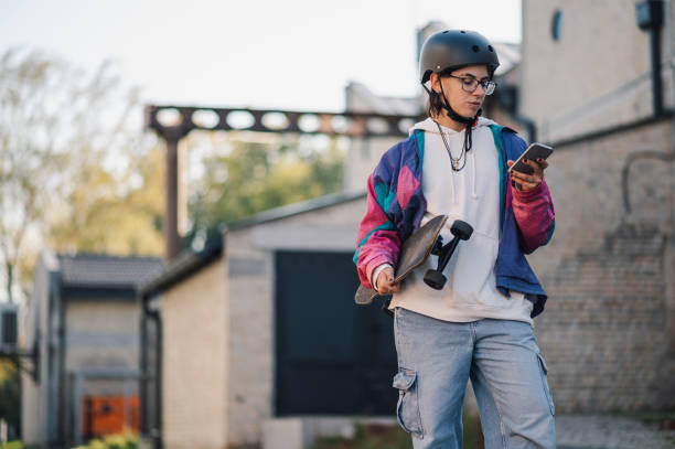 istock Stylish skateboarder using smartphone while holding skateboard outdoors 2189450554