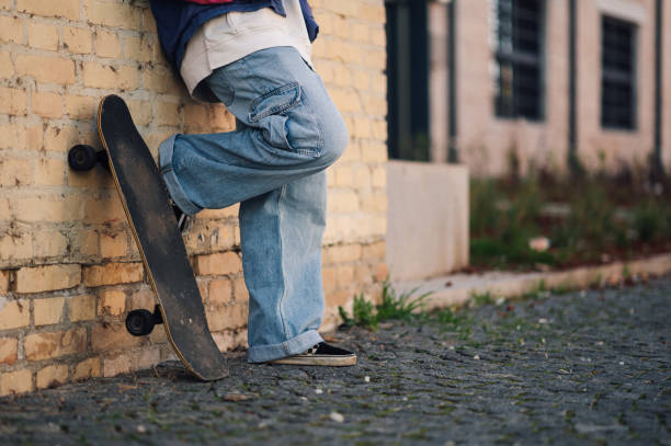 Skateboarder riding on pink skateboard. Close-up of teenager feet wearing jeans and black sneakers skateboarding at street stairs. Leisure activity and extreme sport concept
