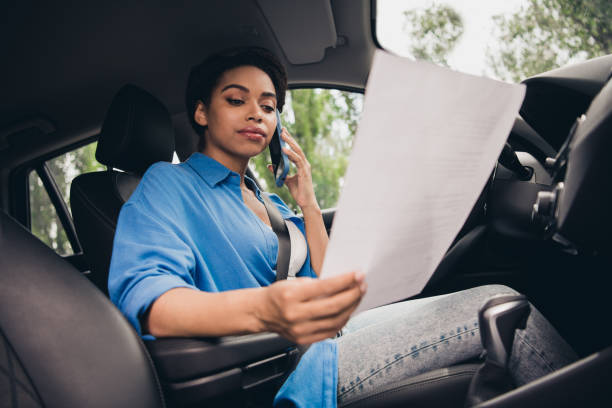 istock Confident young woman driving while on phone call, focusing on paperwork inside car 2189452556