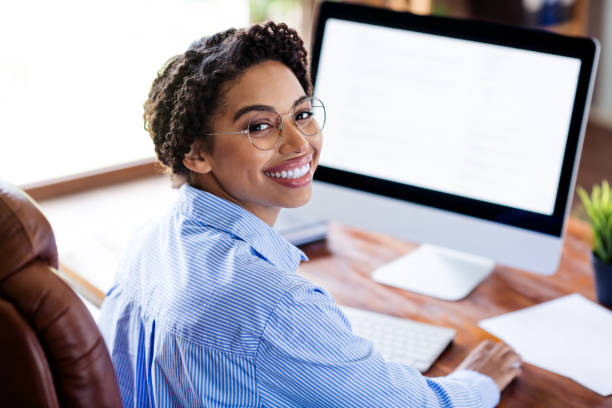 istock Confident young businesswoman in a formal blouse smiles while working on a computer in a modern office setting 2189453491