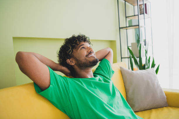 istock Photo of handsome young guy relax sit couch hands behind head dressed green garment spacious house indoors room 2189463146