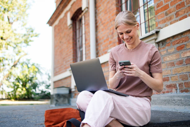 istock Smiling Woman Using Laptop and Smartphone Outdoors at College 2189464405