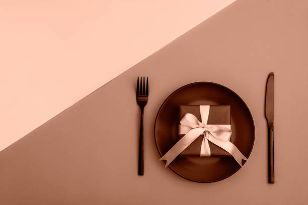 istock Stylish table setting, gift box, plate, cutlery on Mocha Mousse colored background. Demonstrating color of the year 2025. Top view, flat lay 2189471523