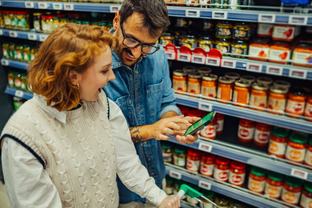 istock Young couple using smartphone while shopping groceries at supermarket 2189472054