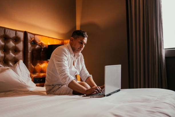 istock Man working on laptop in hotel bed 2189477120