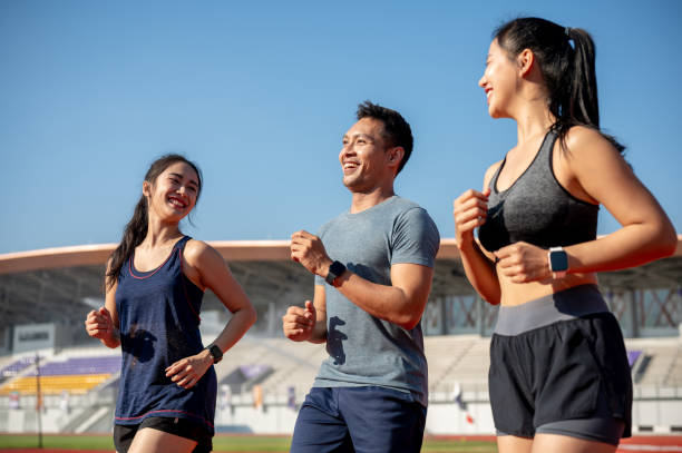 A group of cheerful Asian athlete runners enjoy a conversation while training at a stadium.