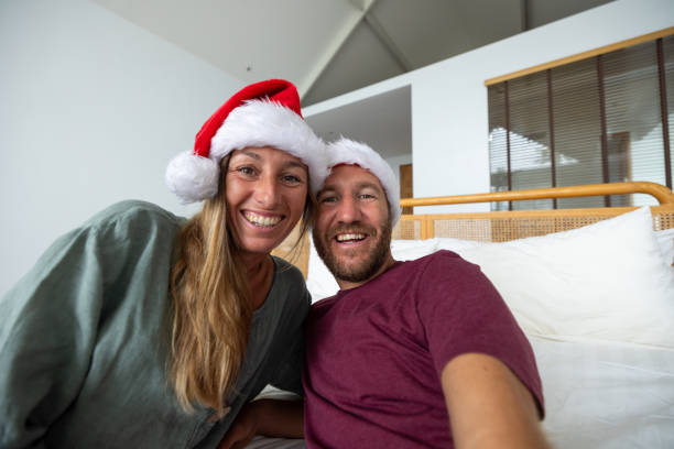 istock Smiling couple wearing Santa hats taking a selfie on bed. 2189496600