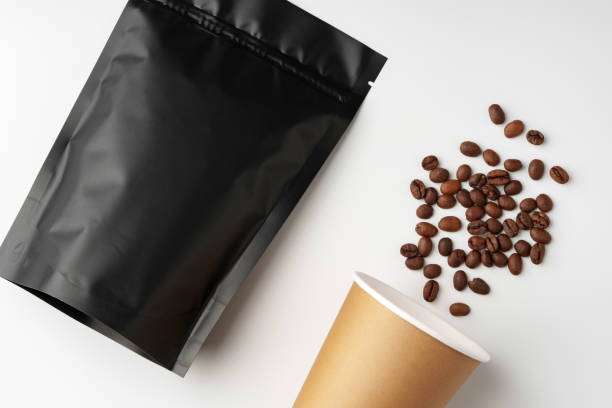 istock Freshly roasted coffee beans beside a takeout cup and black packaging on a white surface 2189513306