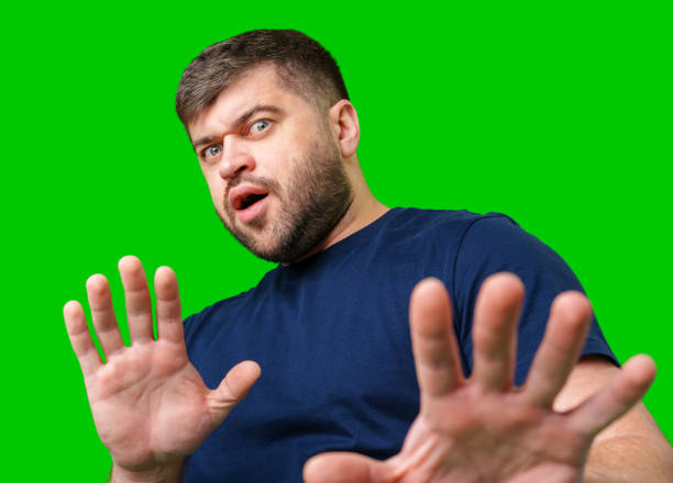 istock A man with a serious expression holds up both hands in a stopping gesture against a bright green background 2189515140