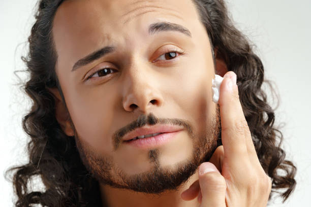 istock A young man applying skincare cream on his face with a focused expression, demonstrating personal grooming at home 2189525924