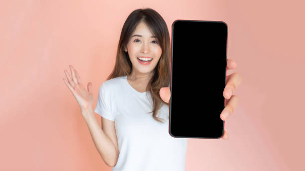 istock beautiful Asian young woman showing big smart phone with blank screen , white screen empty copy space for advertising banner isolated on pink background , Mock Up Image 2189532103