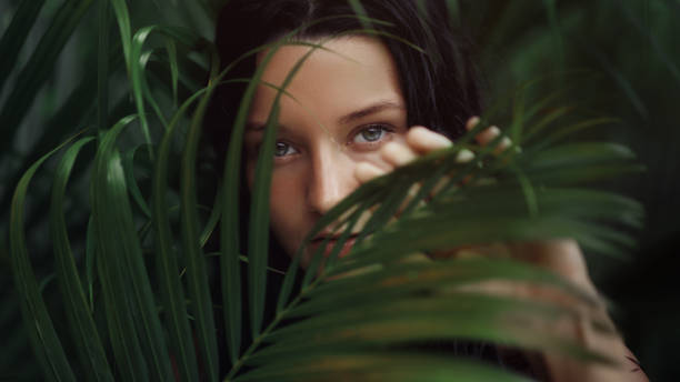 istock Mysterious Woman Peeking Through Tropical Leaves in Lush Greenery 2189532959