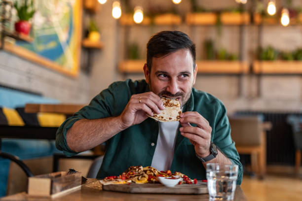 A man savoring a delicious slice of pizza in a chic, modern restaurant. The image captures the pleasure of dining in a trendy setting, where the man enjoys high-quality pizza in a stylish and inviting atmosphere. Ideal for illustrating themes of contemporary dining, gourmet pizza, and the experience of enjoying a meal in an upscale restaurant.