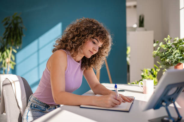 istock Young woman writing in notebook at sunny modern workspace 2189535677