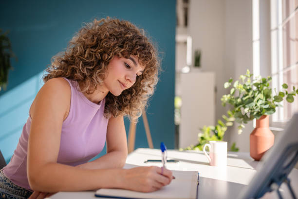 istock Young woman writing notes while enjoying natural light in a cozy workspace 2189535767