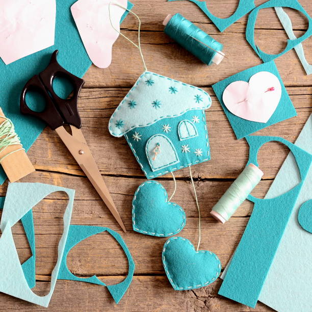 Felt house with hearts decor, tools and materials for sewing crafts, paper patterns on wooden background