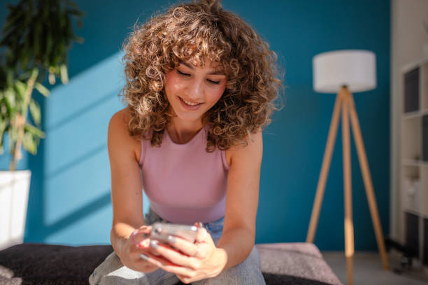 istock Young woman sitting indoors smiling while using her smartphone during daytime 2189536325