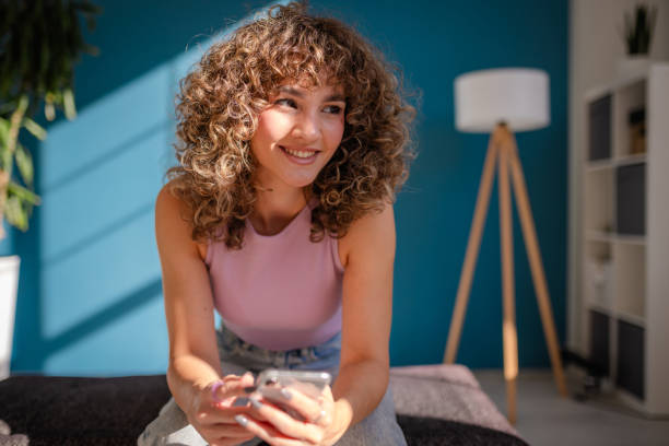 istock Smiling woman with curly hair using smartphone in a modern home interior 2189536363