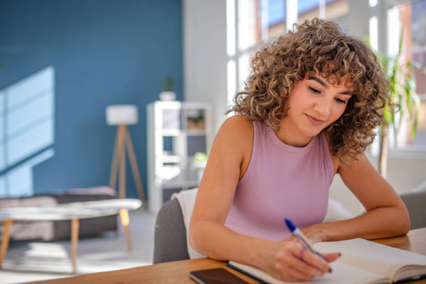 istock Woman writing in a notebook at a desk in a bright home office 2189536601