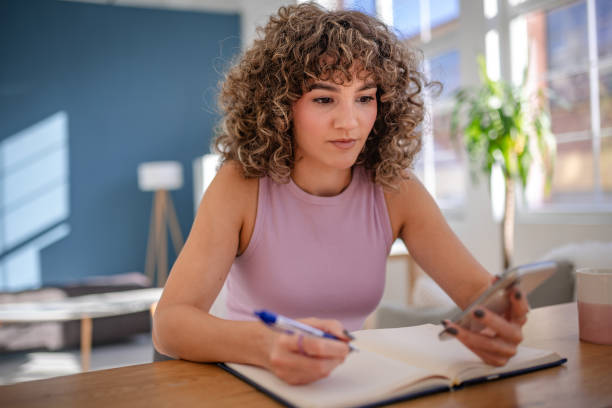 istock Young woman studying at home while researching using a smartphone 2189536665