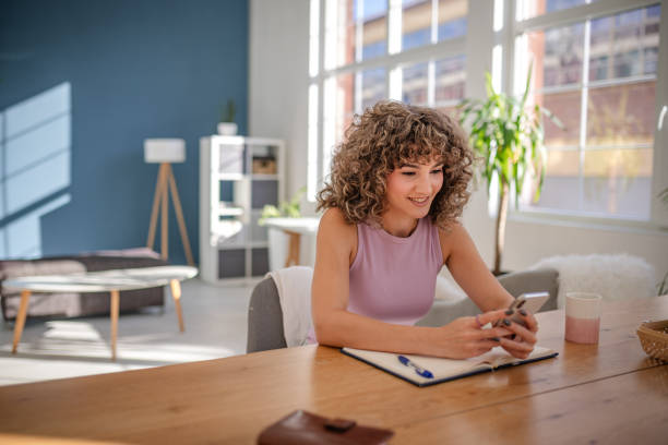 istock Smiling Woman Using Smartphone at Desk with Notebook and Modern Interior Design 2189536713