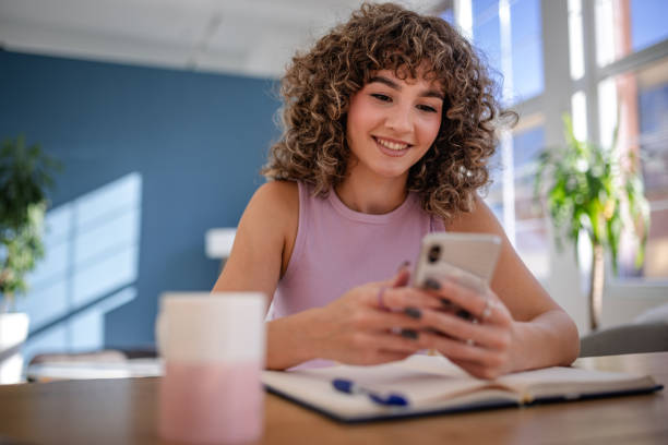 istock Smiling woman using smartphone while working at home during a bright morning 2189537408