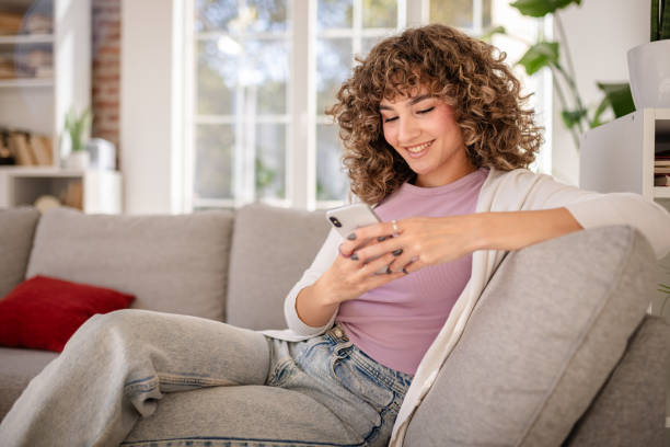istock Young woman smiling while using a smartphone on a cozy couch at home 2189537612