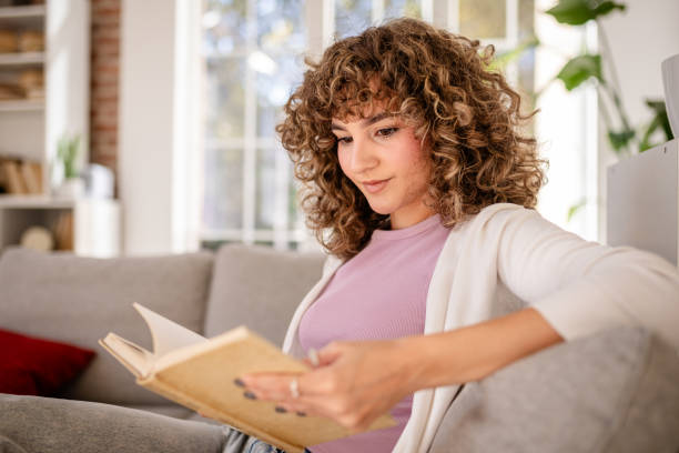 istock Young woman relaxing at home while reading a book in a cozy setting 2189537684