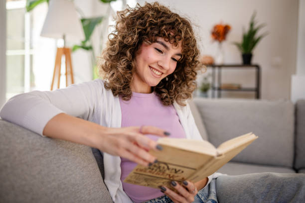 istock Smiling woman reading a book while relaxing on a cozy living room sofa 2189537882