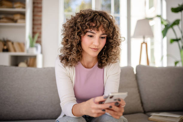 istock Woman with curly hair using smartphone while sitting on a comfortable couch 2189538076