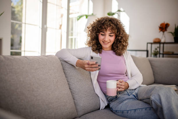 istock Woman sitting on a sofa using smartphone while holding a coffee mug 2189538444