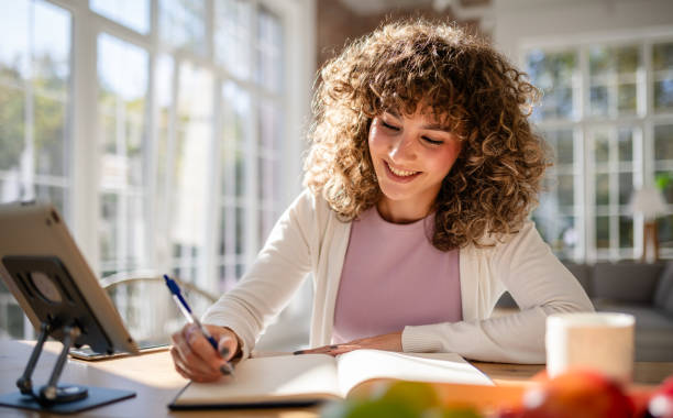 Woman writing in a journal while smiling in a bright modern home