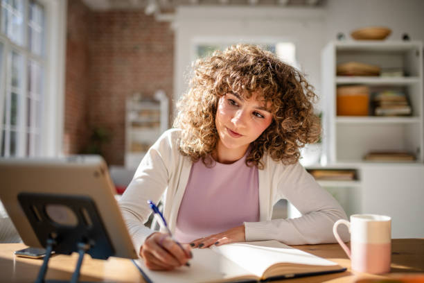 istock Young woman studying and writing notes at a desk indoors 2189540575