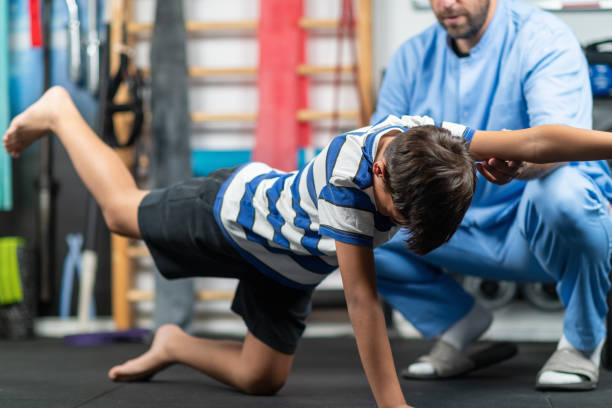 istock Physical therapist instructing a young boy in exercises, focusing on improving mobility, strength, and balance during a personalized rehabilitation session 2189541407