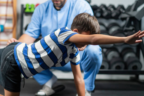 istock Physical therapist guiding a young boy through exercises for stability and balance, aimed at improving coordination and strength in a supportive rehabilitation session 2189541527