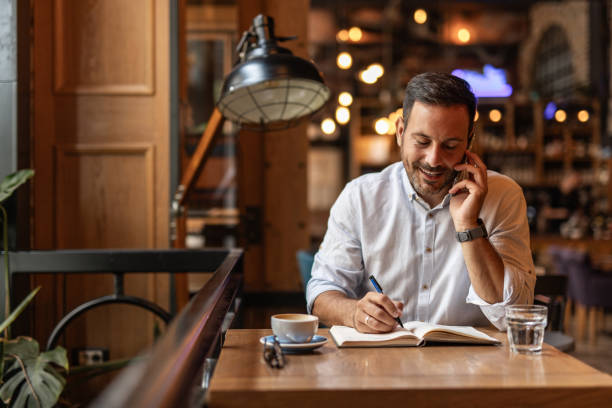 istock Businessman in a cafe - Drinking coffee, talking on the phone, and writing notes 2189557053