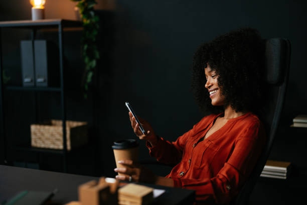 istock Smiling young woman using mobile phone and drinking coffee in office 2189558099