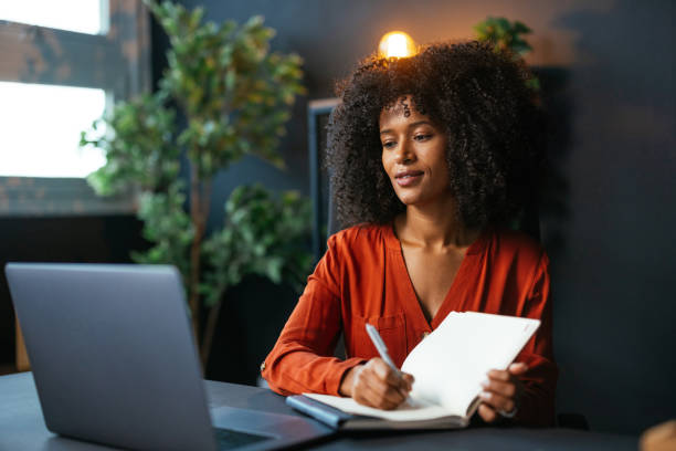 istock Focused young woman taking notes while working on laptop in modern office 2189558133