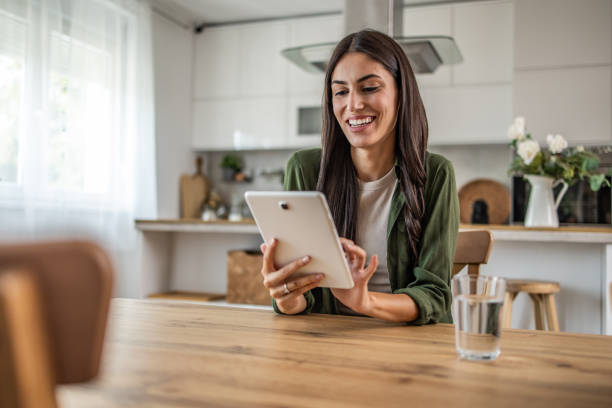 Smiling young woman using digital tablet while sitting at table in dining room