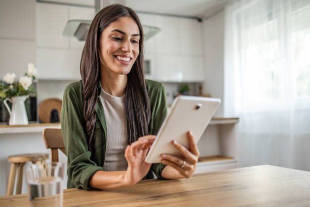 istock Smiling young woman using digital tablet while sitting at table in dining room 2189560480
