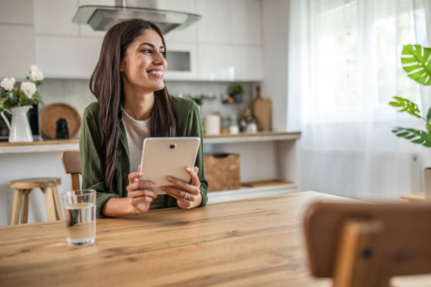 istock Smiling young woman using digital tablet while sitting at table in dining room 2189560487